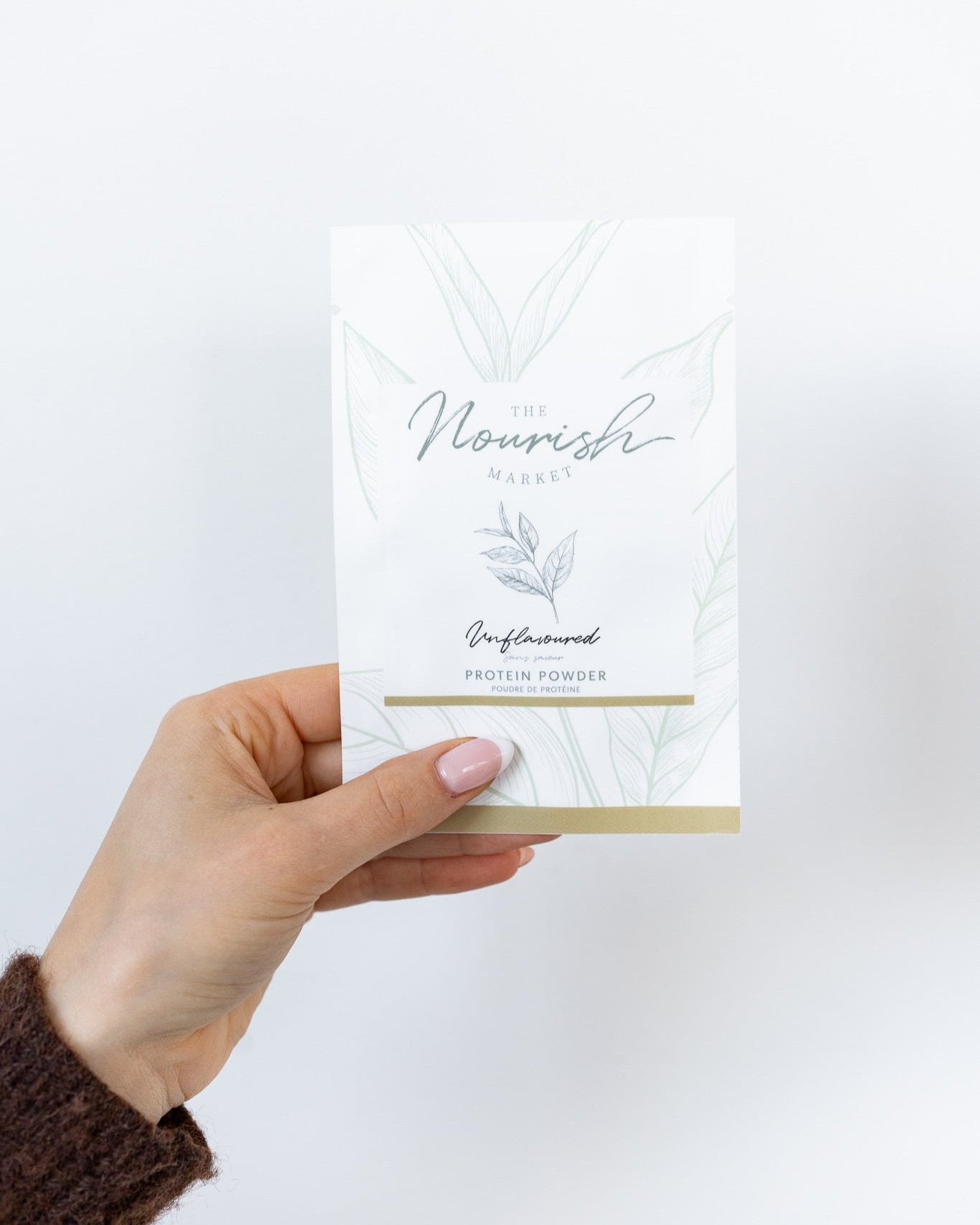 A hand holding up a sample pack of unflavoured protein powder.